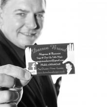 Wedding Magician Darren Brand appears here in a black-and-white photograph wearing a smart suit and holding out his business card close to the camera